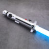 Studio mockup of the silver Snips CW shoto saber hilt, highlighting its minimalist profile, black buttons, and blue blade ignition, set against a dark futuristic background with a blue monkey mascot icon.