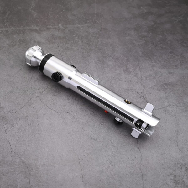 A silver Snips CW shoto saber hilt by Laser Monkey Sabers, featuring a minimalist design with black buttons and a rounded pommel, resting on a gray concrete surface.